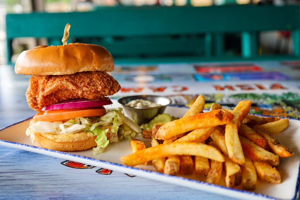 A close-up view of a crispy fried chicken sandwich with lettuce, tomato, and onion, served with seasoned french fries and dipping sauce on a restaurant table.