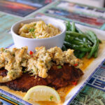 A close-up view of a blackened fish fillet topped with crab stuffing, served with a side of rotini pasta and green beans on a restaurant table.