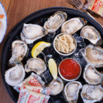 An overhead view of a raw oyster platter on ice with cocktail sauce, horseradish, lemon wedges, and saltine crackers.