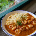 A close-up view of a bowl of creamy grits with shredded parmesan cheese and sautéed shrimp in a rich savory gravy.