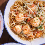 A top-down view of shrimp pasta garnished with shredded parmesan cheese and diced tomatoes in a blue-rimmed bowl.