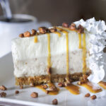 piece of cheesecake on a plate with pralines, whipped cream and sauce