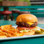 closeup of burger on plate with cheese, lettuce and tomato side of fries