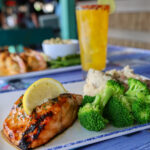 grilled salmon on plate with broccoli and potatoes as side dishes and drink in the background
