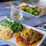 piece of grouper on plate with pistachios crusted on top, green beans and grits as a side dish