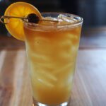 yellow drink with floater and a cherry orange garnish