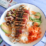 pink sliced tuna on a bed of white rice, carrots, cucumbers and avocado