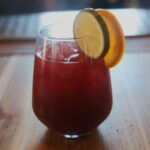 red drink in a wine glass with lime and orange wheel garnish